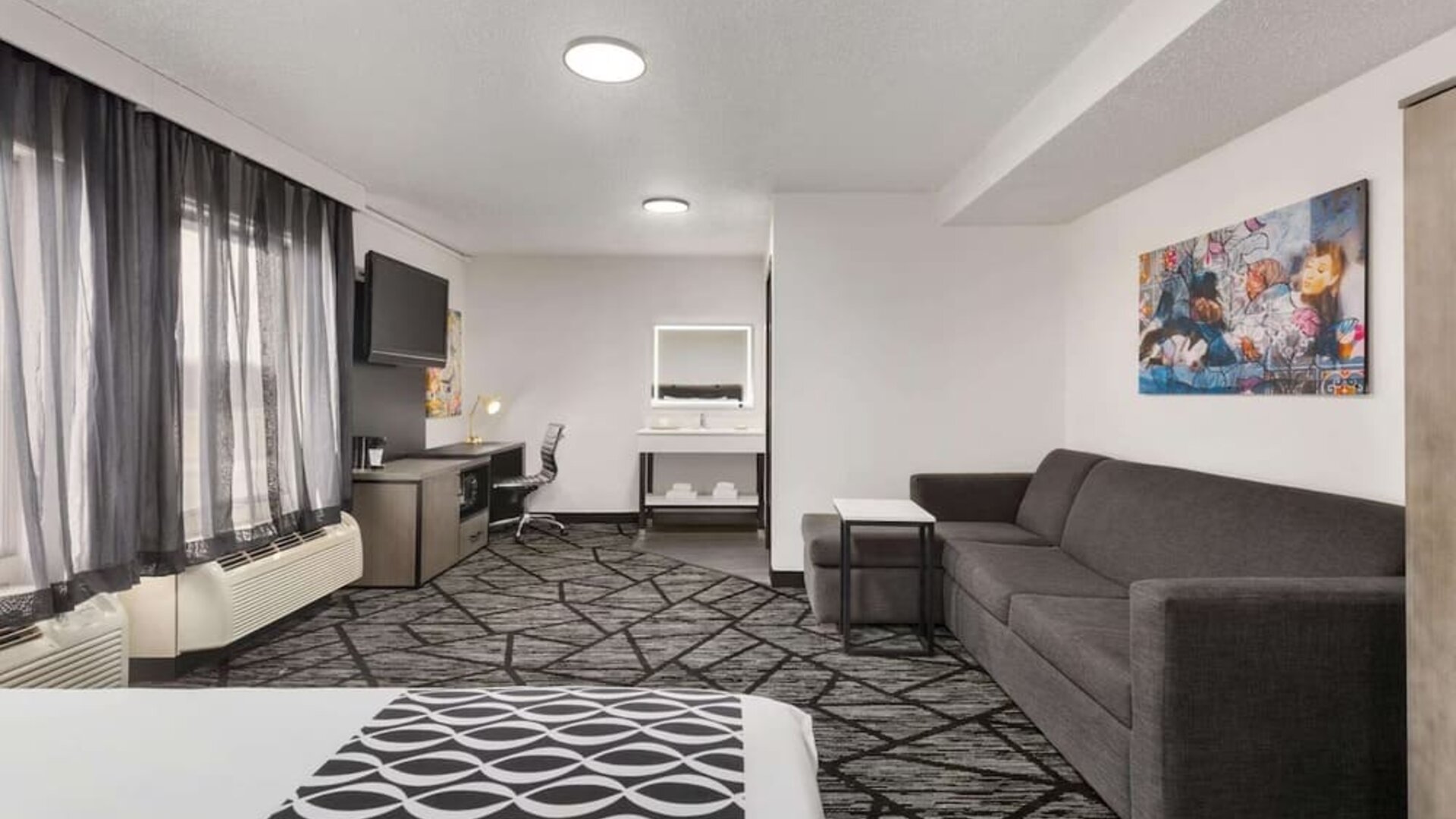 Spacious guest room featuring a bed, sofa seating area, work desk, television, and large windows at La Quinta Inn & Suites By Wyndham Cleveland Airport West.