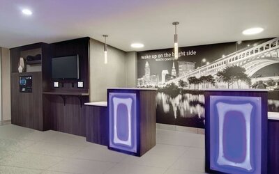 Modern reception area featuring illuminated front desks and a Cleveland cityscape mural at La Quinta Inn & Suites By Wyndham Cleveland Airport West.