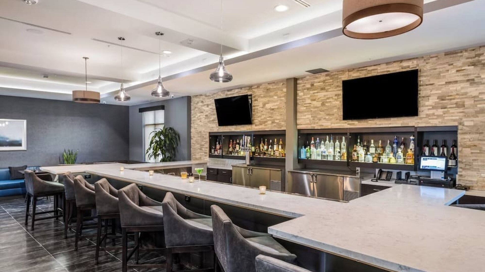 Contemporary hotel bar featuring a spacious counter, comfortable bar seating, televisions, and a selection of beverages at Holiday Inn & Suites Silicon Valley - Milpitas.