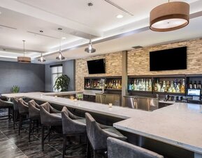 Contemporary hotel bar featuring a spacious counter, comfortable bar seating, televisions, and a selection of beverages at Holiday Inn & Suites Silicon Valley - Milpitas.
