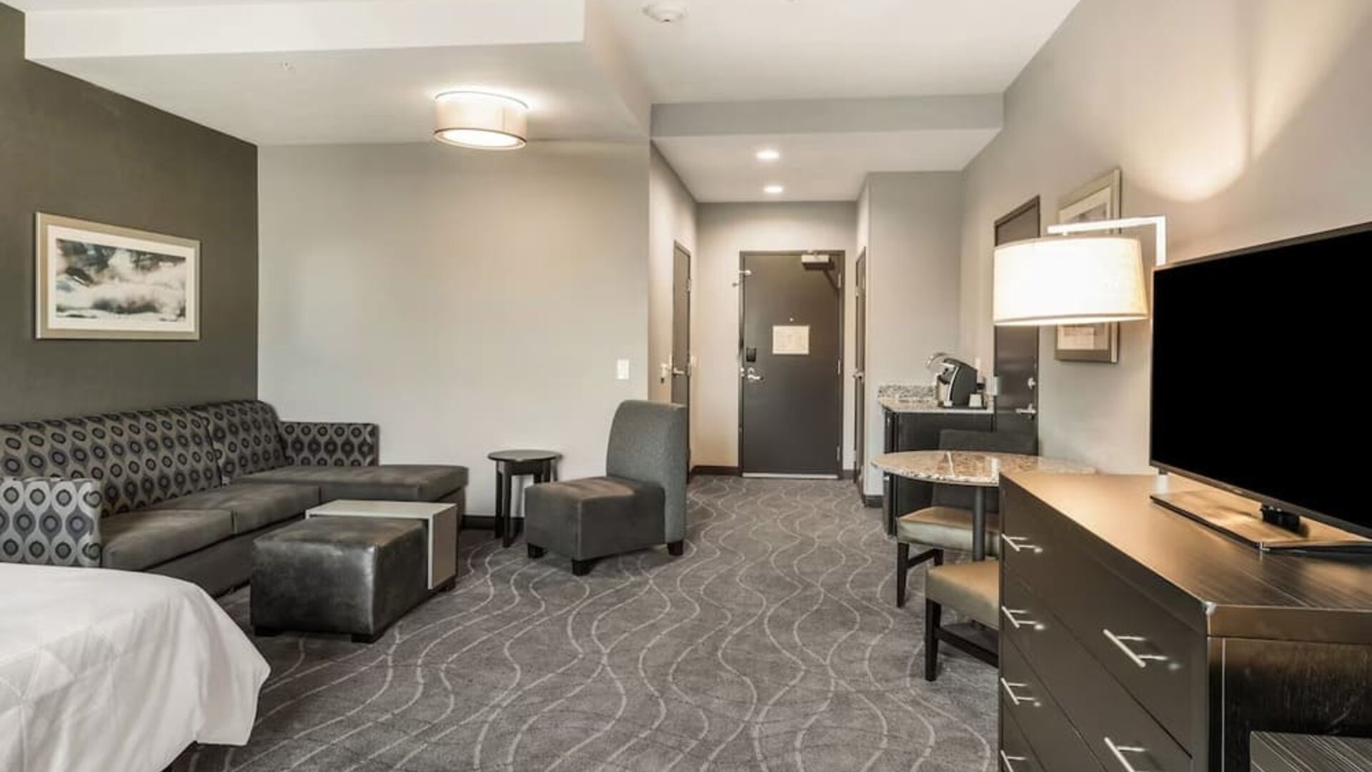 Spacious guest room lounge area featuring sofa seating, armchairs, television, dining space, and modern furnishings at Holiday Inn & Suites Silicon Valley - Milpitas.
