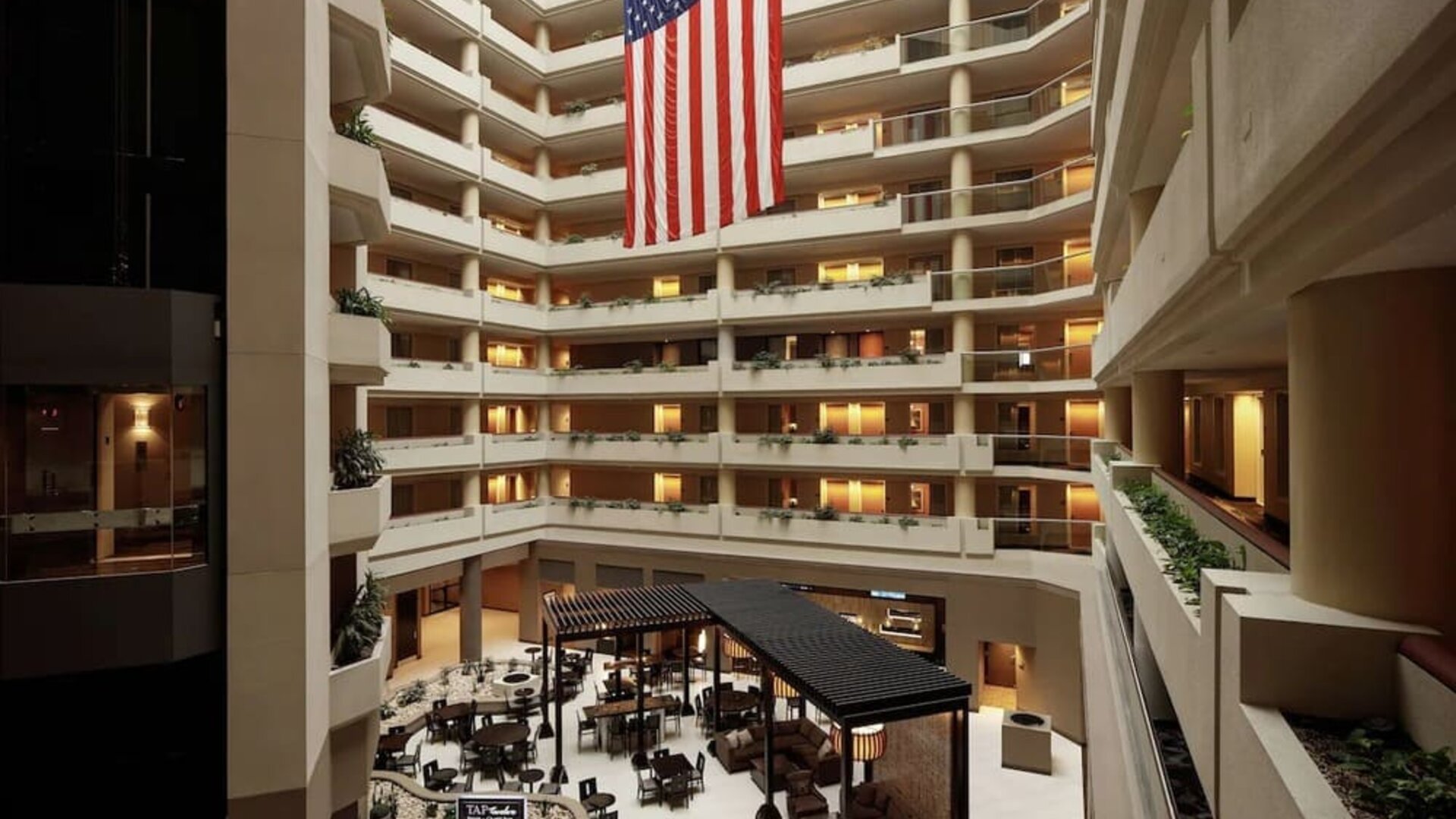Impressive multi-storey atrium featuring open balconies, lounge seating, dining areas, and a large American flag at Embassy Suites by Hilton Crystal City National Airport.