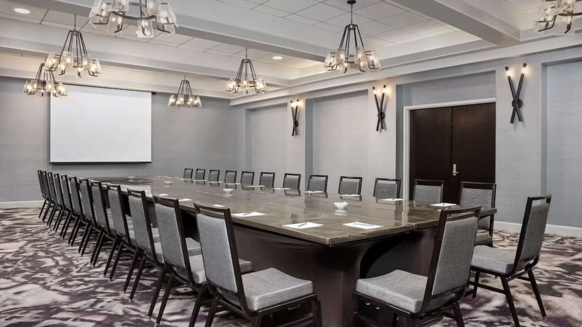 Spacious boardroom featuring a large conference table, ample seating, presentation screen, and contemporary lighting at Embassy Suites by Hilton Crystal City National Airport.