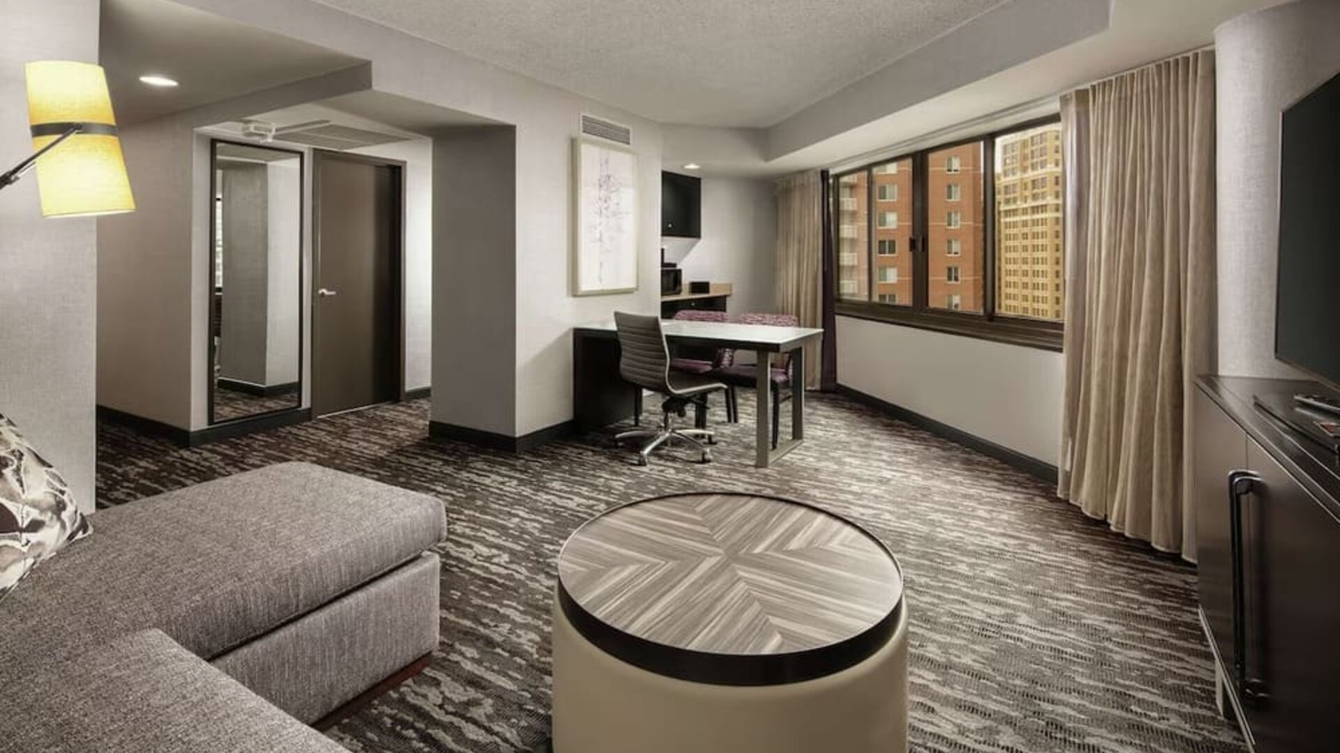 Spacious suite lounge area featuring sofa seating, a work and dining table, television, and large windows at Embassy Suites by Hilton Crystal City National Airport.