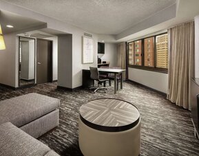 Spacious suite lounge area featuring sofa seating, a work and dining table, television, and large windows at Embassy Suites by Hilton Crystal City National Airport.