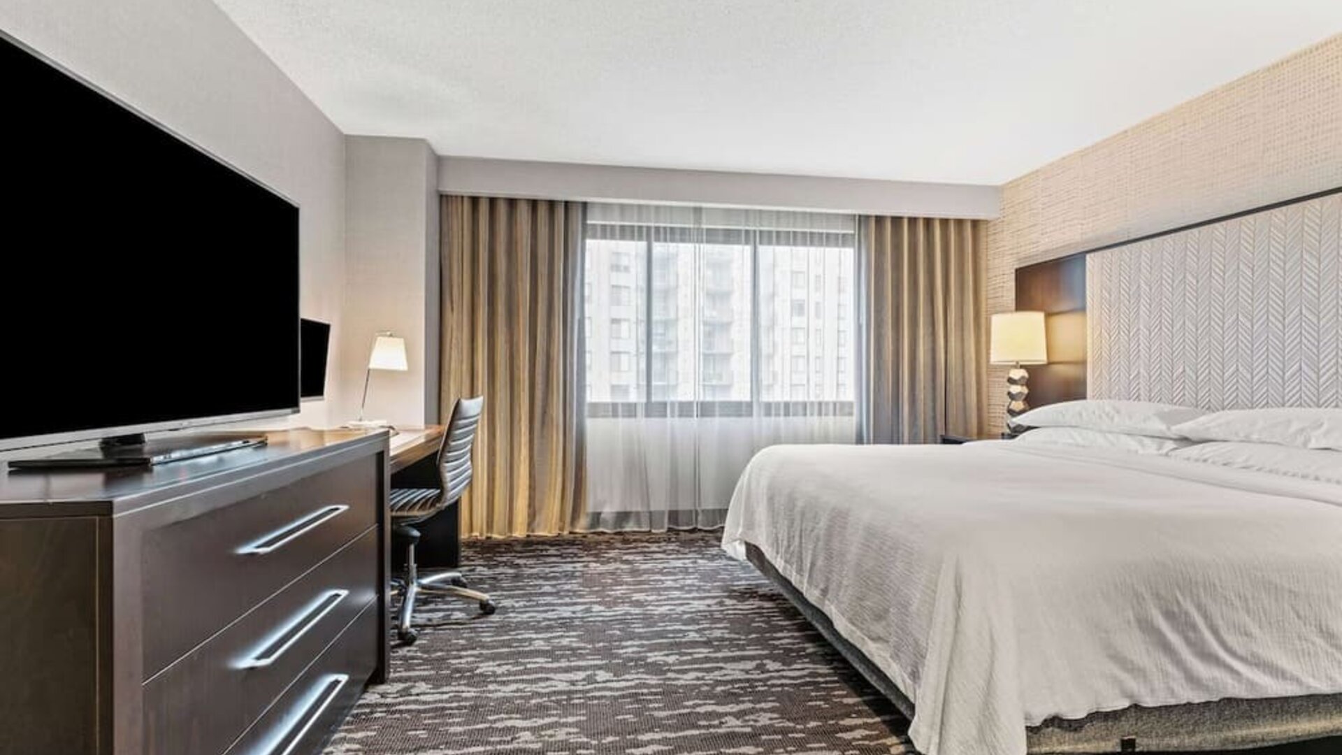 Bright king guest room featuring a comfortable bed, workspace, television, and ample natural light from a large window at Embassy Suites by Hilton Crystal City National Airport.