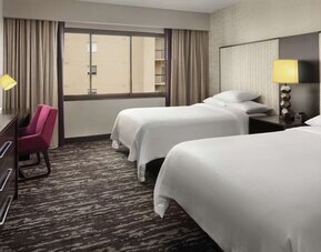 Comfortable guest room featuring two beds, dedicated workspace, television, large window, and contemporary décor at Embassy Suites by Hilton Crystal City National Airport.