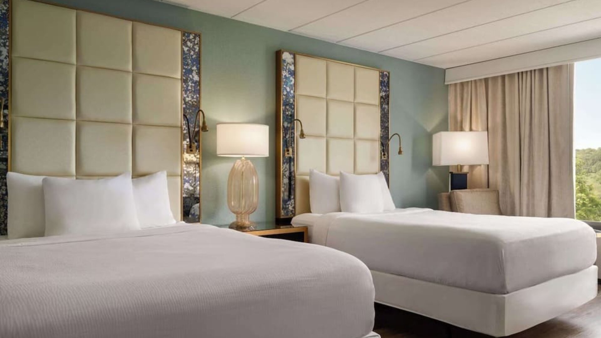 Comfortable guest room featuring two beds, modern headboards, bedside lighting, an armchair, and large window at Wyndham Garden Pittsburgh Airport.