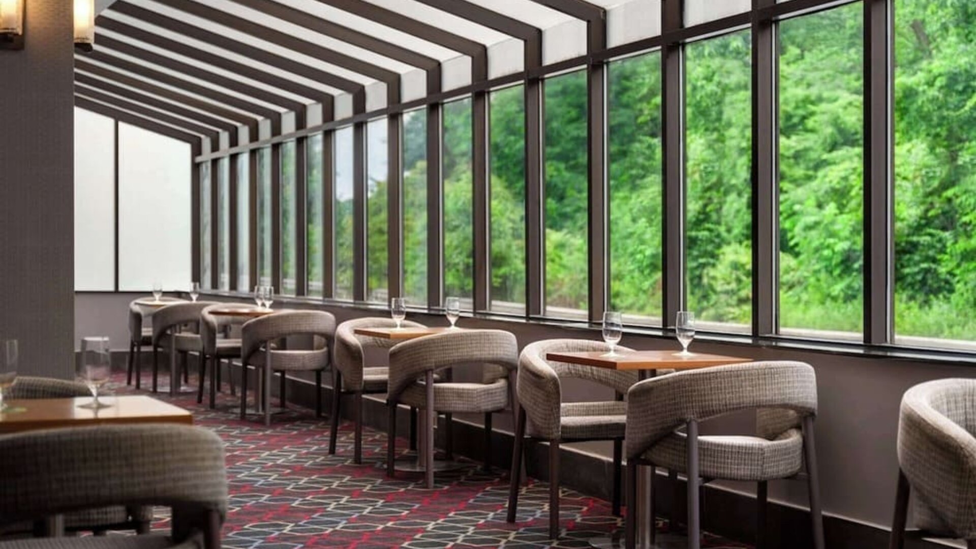 Bright dining area featuring comfortable seating, individual tables, and floor-to-ceiling windows overlooking greenery at Wyndham Garden Pittsburgh Airport.