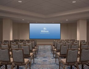Hotel conference room arranged theater-style with rows of upholstered chairs facing a large presentation screen displaying the Hilton Orlando Buena Vista Palace logo.