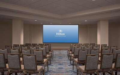 Hotel conference room arranged theater-style with rows of upholstered chairs facing a large presentation screen displaying the Hilton Orlando Buena Vista Palace logo.