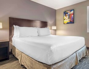 Comfortable king guest room featuring a large bed, bedside lighting, shuttered window, and colourful wall art. Best Western McCarran Inn.