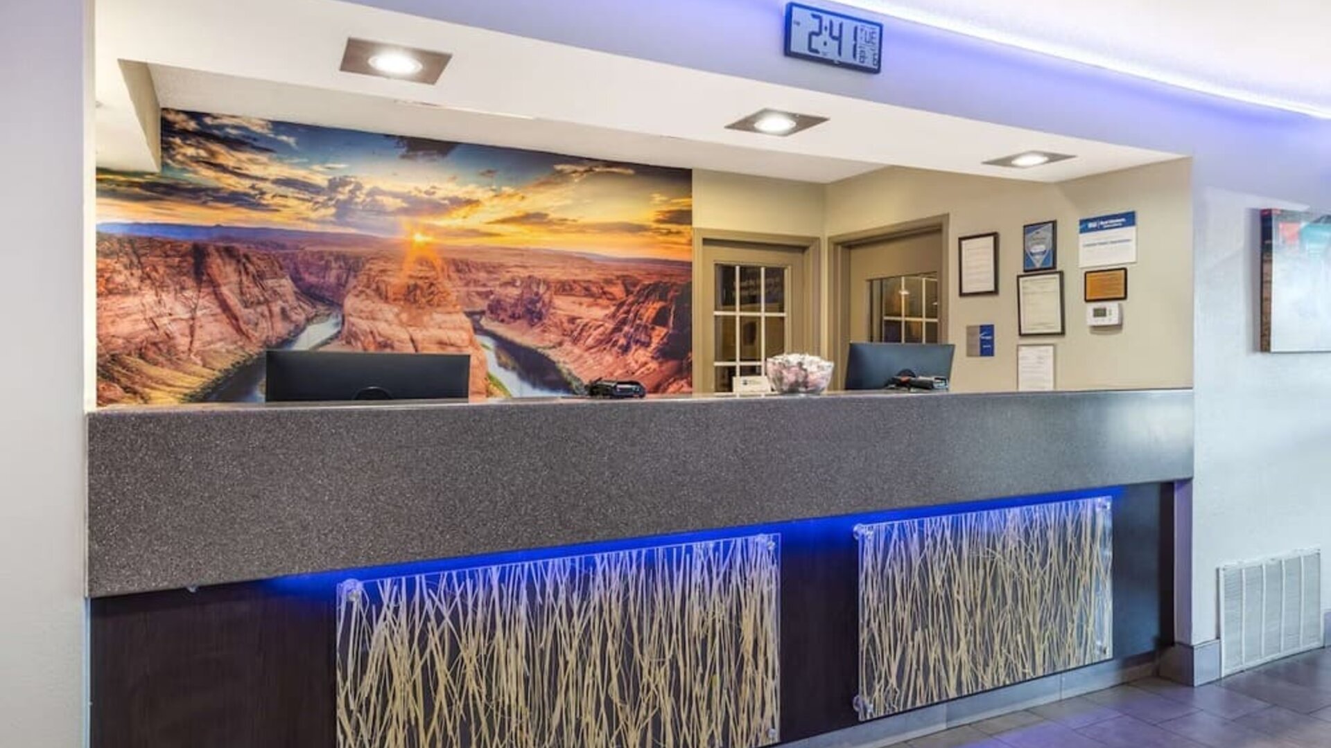 Reception desk featuring contemporary lighting, computer stations, decorative panels, and a scenic canyon mural. Best Western McCarran Inn.