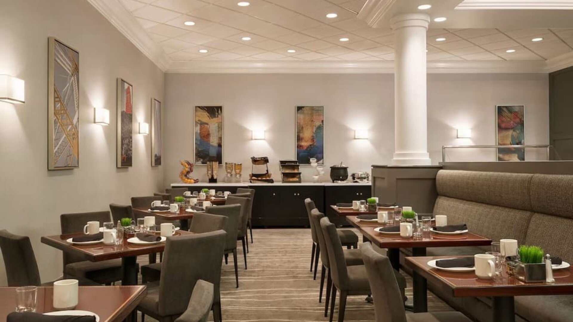 Dining area featuring set tables, upholstered seating, buffet station, and contemporary wall art. Crowne Plaza Englewood.