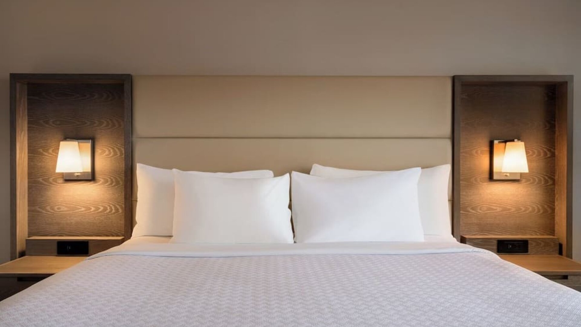 King guest room featuring a large bed with padded headboard, bedside tables, and integrated reading lights. Crowne Plaza Englewood.