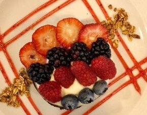 Elegant dessert topped with fresh strawberries, raspberries, blackberries and blueberries with decorative fruit sauce. LaiLa Hotel CDMX.