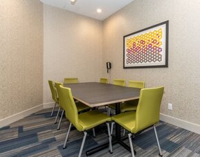 Private hotel meeting room with a rectangular conference table, eight green chairs, patterned carpet, wall-mounted telephone, and colorful framed artwork.