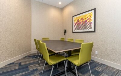 Private hotel meeting room with a rectangular conference table, eight green chairs, patterned carpet, wall-mounted telephone, and colorful framed artwork.