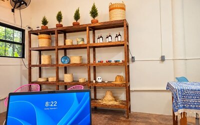 Bright coworking space with wooden shelving displaying woven baskets, small potted plants, ceramics, and bottles, with a computer workstation in the foreground.