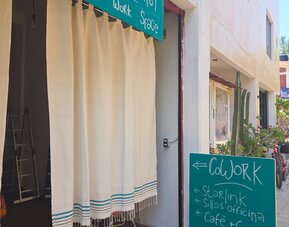 Entrance to a zen coworking space with white curtains and turquoise signs advertising Wi-Fi, office chairs, café food, and a half-day coworking rate.