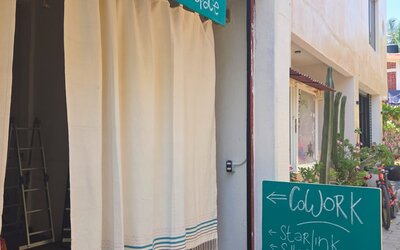 Entrance to a zen coworking space with white curtains and turquoise signs advertising Wi-Fi, office chairs, café food, and a half-day coworking rate.