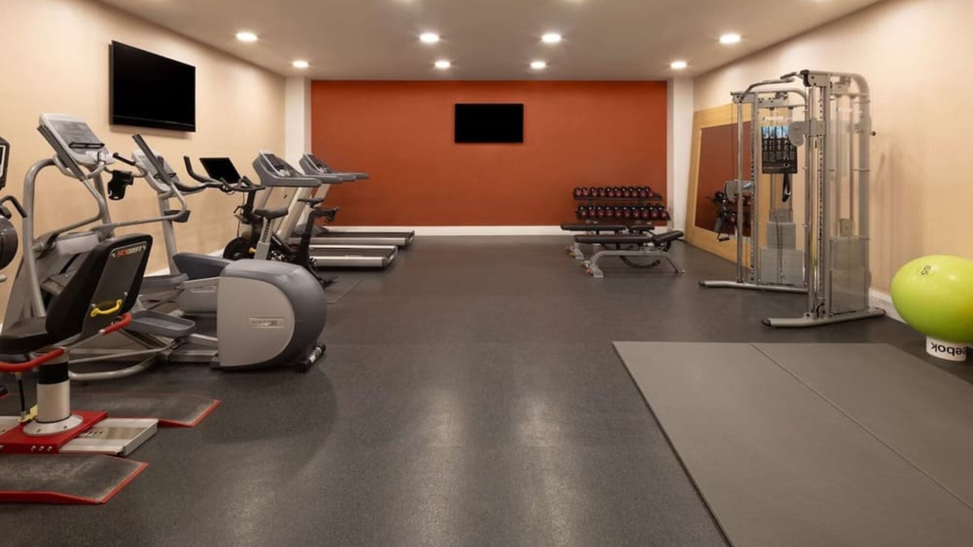 Spacious hotel fitness center with treadmills, elliptical machines, exercise bikes, dumbbells, weight-training equipment, exercise mats and stability balls.