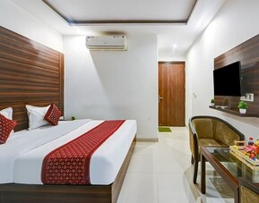 Contemporary hotel room with a large bed featuring white linens and red patterned accents, dark wood wall panels, wall-mounted TV, air conditioning, upholstered seating and a glass table with refreshments.