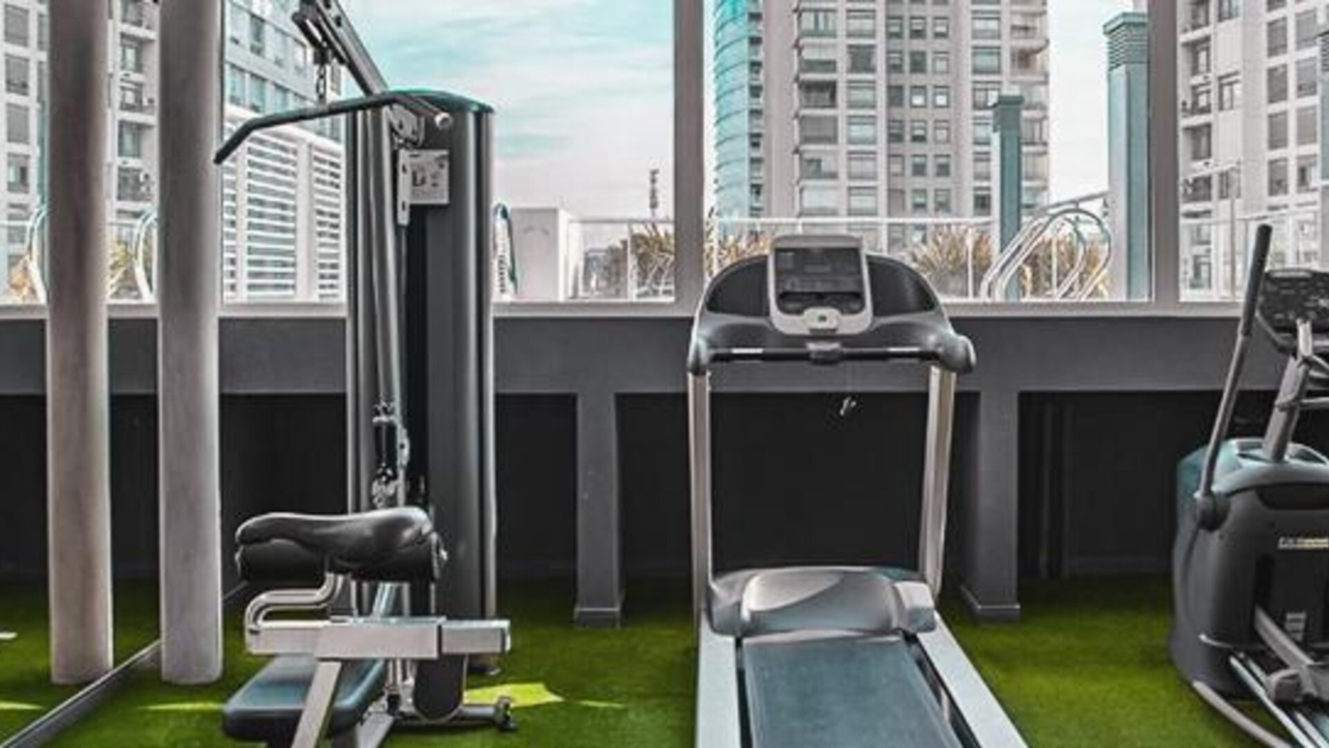 Fitness center with cardio and strength equipment, artificial grass flooring, and city views at Dazzler by Wyndham Polo.