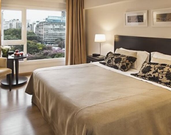 King-bed guest room with a large window overlooking city buildings, armchair, television, and bedside tables at El Conquistador Hotel.