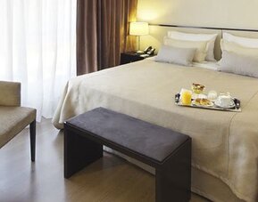 Guest room with a king bed, armchair, bench, bedside tables, lamps, and breakfast tray at El Conquistador Hotel.
