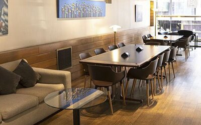 Lounge and dining area with a long table, chairs, sofa, artwork, and windows overlooking the street at El Conquistador Hotel.