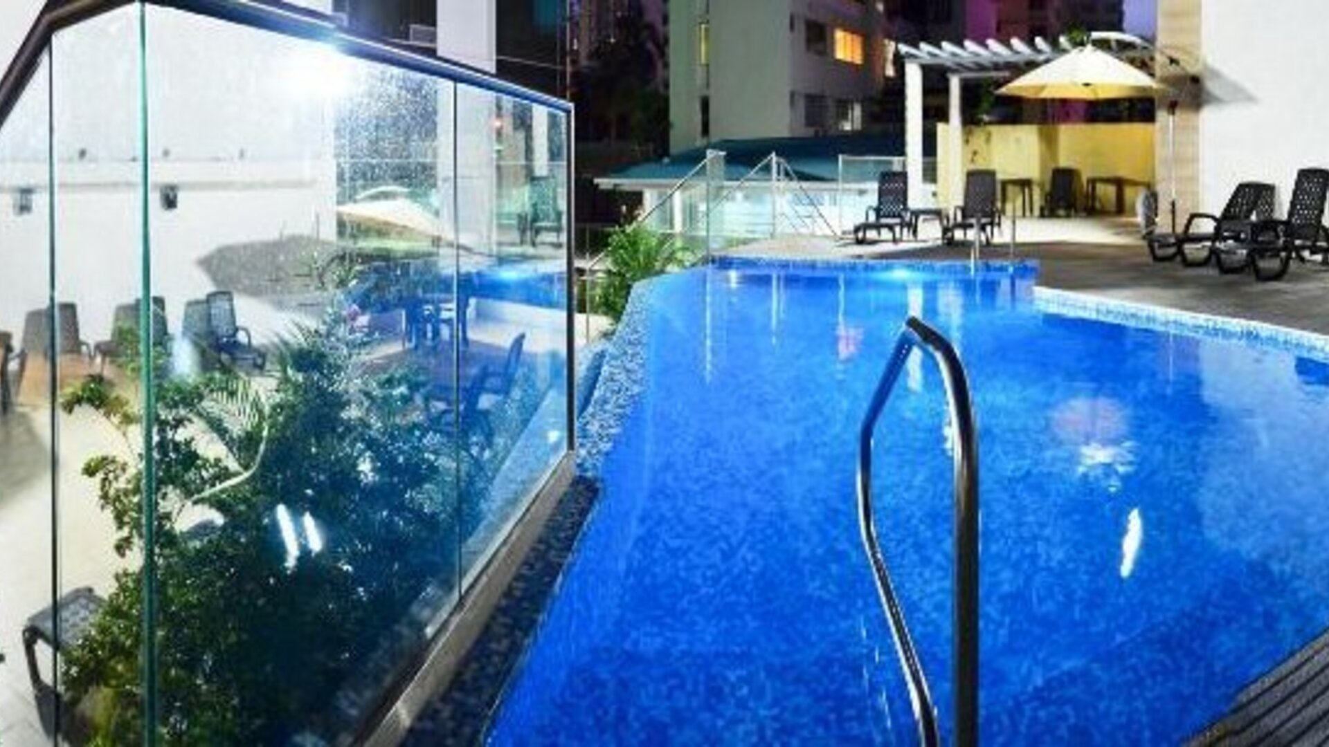 Outdoor swimming pool with blue water, glass panels, lounge chairs, and umbrellas at Hotel Grand International.