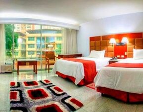Guest room with two beds, red runners, seating area, patterned rug, and large windows overlooking the surroundings at Hotel Grand International.