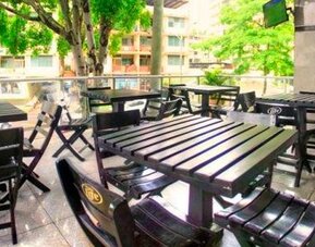 Outdoor terrace with black tables and chairs overlooking trees and surrounding buildings at Hotel Grand International.