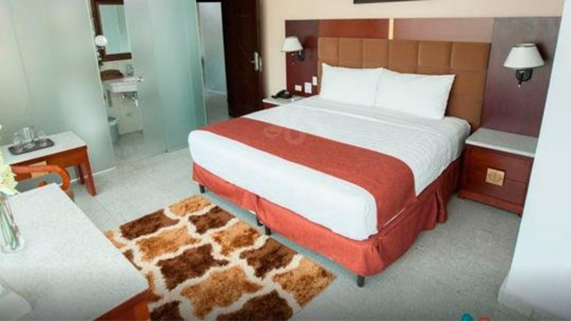 Guest room with a king bed, red runner, padded headboard, bedside tables, and patterned rug at Hotel Grand International.