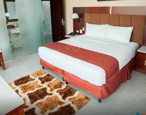Guest room with a king bed, red runner, padded headboard, bedside tables, and patterned rug at Hotel Grand International.