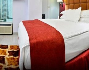 Guest room with a king bed, red runner, wood furnishings, desk, and large windows overlooking city buildings at Hotel Grand International.