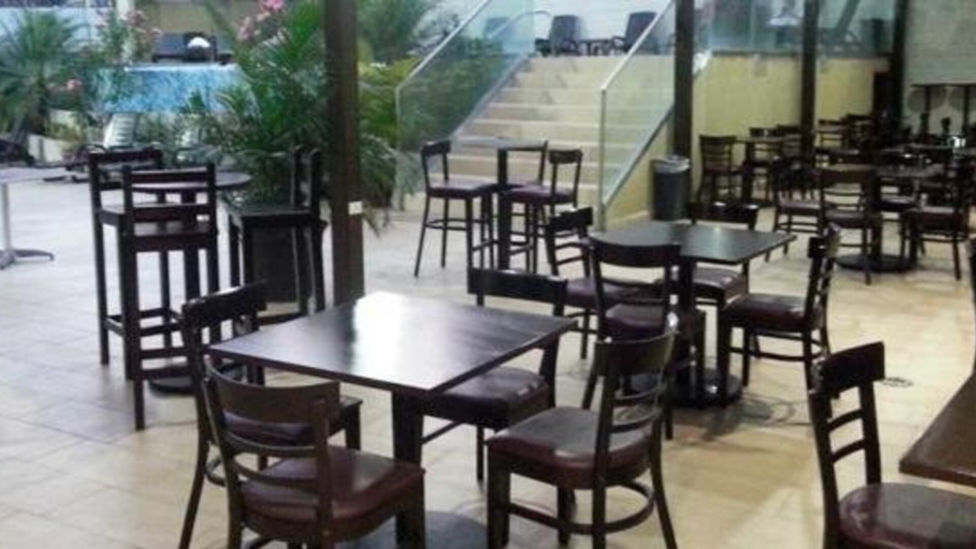 Indoor dining area with dark wooden tables and chairs beside large windows overlooking an outdoor pool at Hotel Grand International.