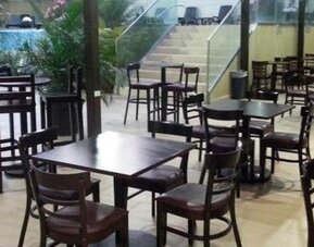 Indoor dining area with dark wooden tables and chairs beside large windows overlooking an outdoor pool at Hotel Grand International.