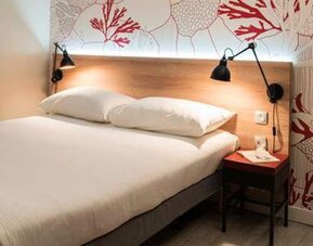 Guest room with a double bed, coral-patterned wall, bedside table, wardrobe, and mirrored closet at Hotel ibis Styles Barcelona City Bogatell.