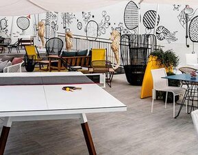 Leisure area with a table tennis table, colorful chairs, tables, and illustrated wall murals at Hotel ibis Styles Barcelona City Bogatell.