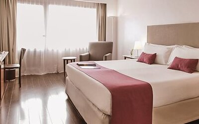 Guest room with a king bed, pink runner and pillows, armchair, desk, bedside tables, and large window at Dazzler by Wyndham Buenos Aires Recoleta.