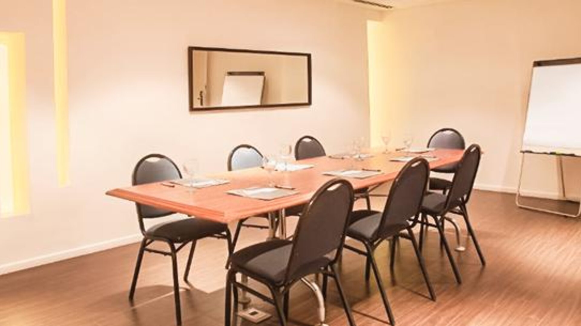 Meeting room with a rectangular table, chairs, notepads, wall mirror, and flip chart at Dazzler by Wyndham Buenos Aires Recoleta.