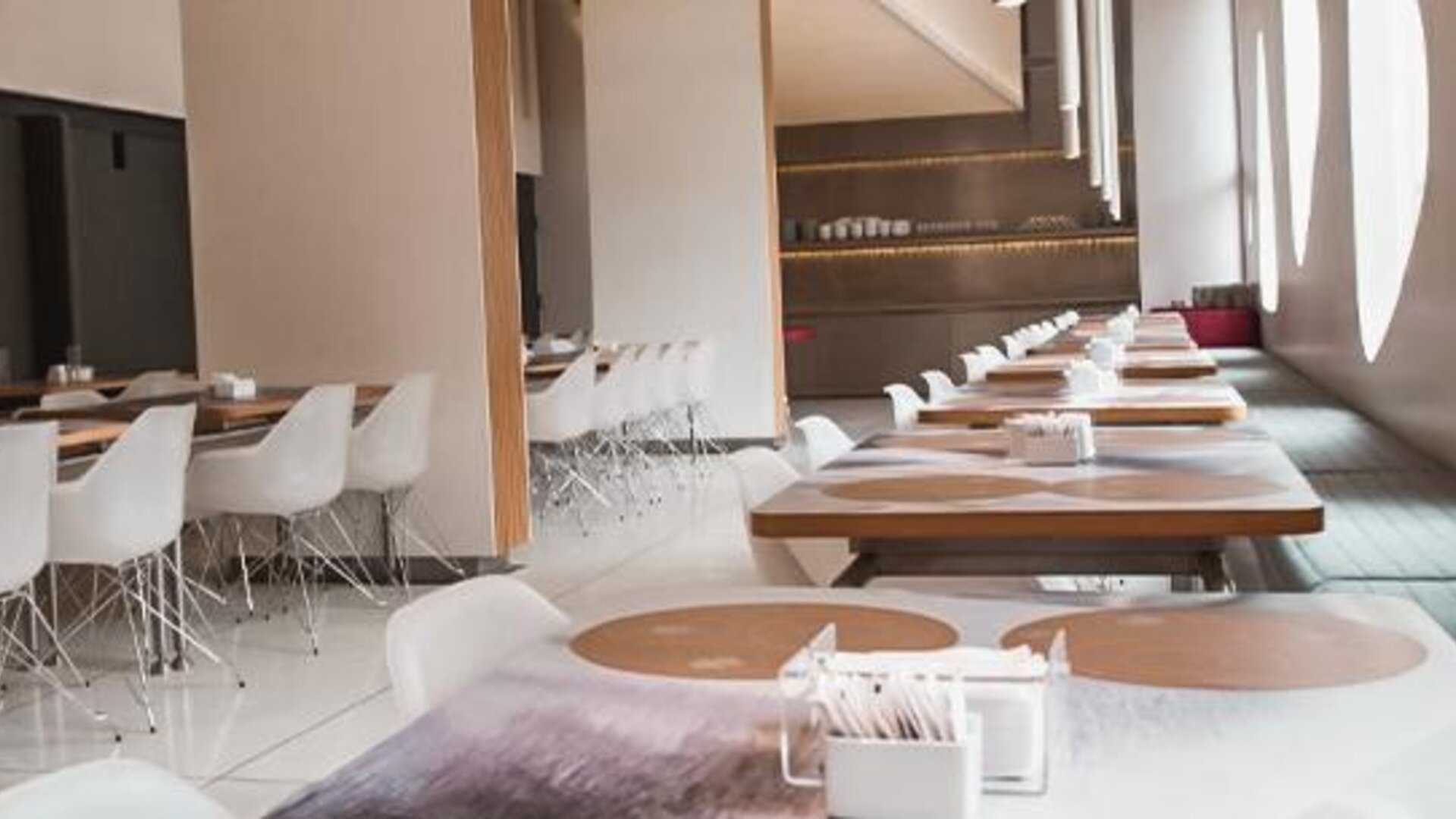 Bright restaurant dining area with wooden tables, white chairs, place settings, and large oval windows at Dazzler by Wyndham Buenos Aires Recoleta.