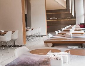 Bright restaurant dining area with wooden tables, white chairs, place settings, and large oval windows at Dazzler by Wyndham Buenos Aires Recoleta.