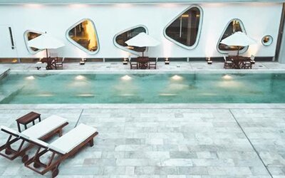 Indoor swimming pool with tiled deck, loungers, tables, umbrellas, and curved windows at Dazzler by Wyndham Buenos Aires Recoleta.