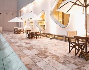 Indoor pool terrace with tables, chairs, umbrellas, curved windows, and poolside seating at Dazzler by Wyndham Buenos Aires Recoleta.