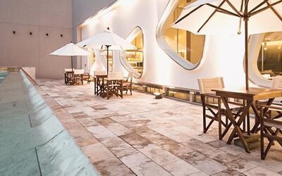 Indoor pool terrace with tables, chairs, umbrellas, curved windows, and poolside seating at Dazzler by Wyndham Buenos Aires Recoleta.