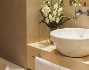 Bathroom with a white vessel sink, bathtub, wall-mounted faucet, toiletries, and floral arrangement at Dazzler by Wyndham Buenos Aires Recoleta.