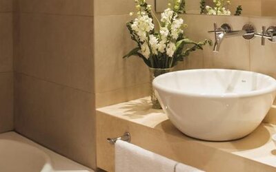 Bathroom with a white vessel sink, bathtub, wall-mounted faucet, toiletries, and floral arrangement at Dazzler by Wyndham Buenos Aires Recoleta.